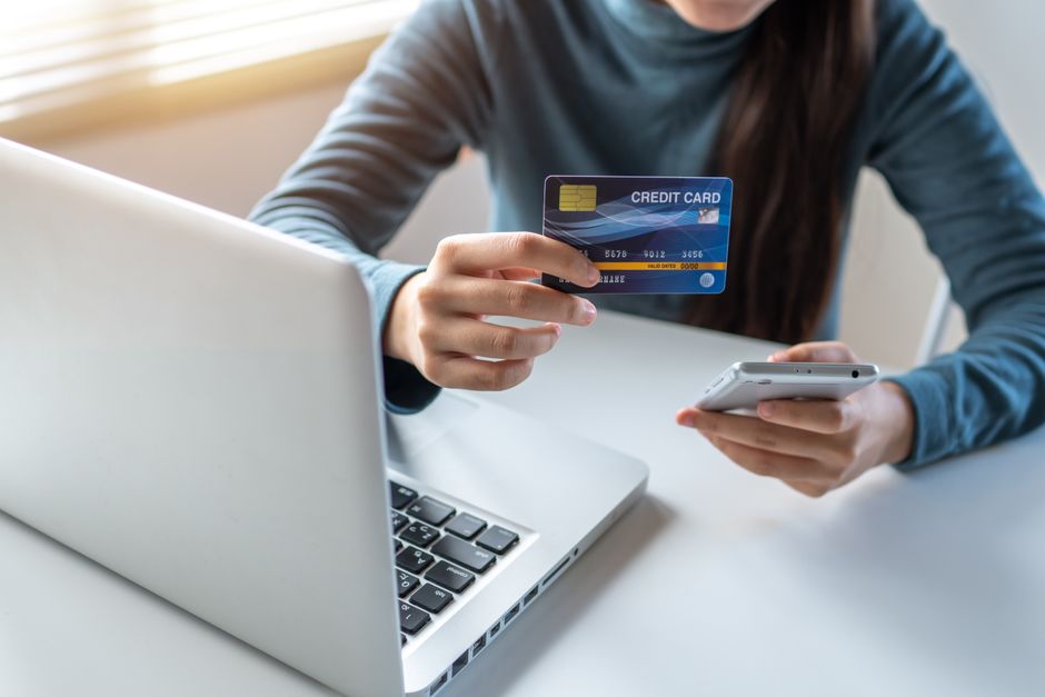 A woman uses a credit card and smartphone for online shopping on her laptop